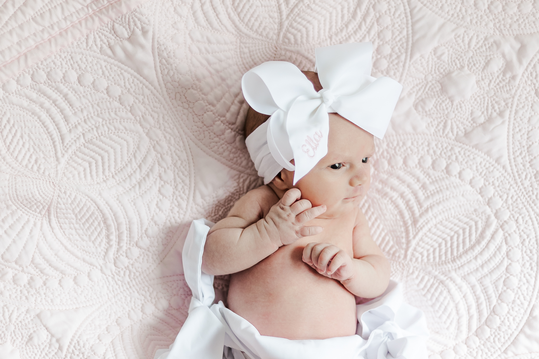 Baby girl in white diaper cover and white bow laying on pink blanket