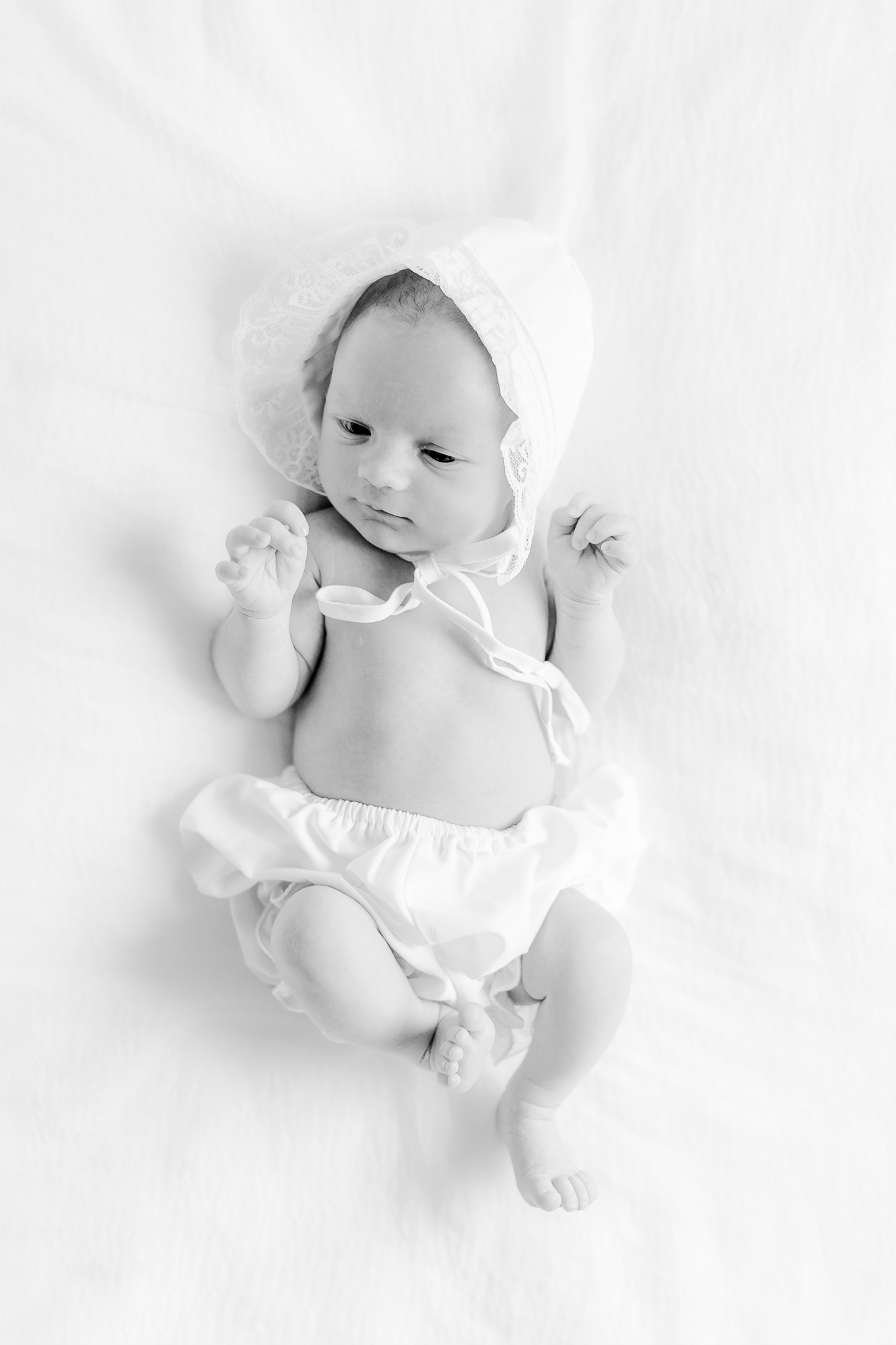 black and white picture of baby girl in ruffle bloomers and bonnet lying on blanket at home in calera Alabama during in-home newborn session