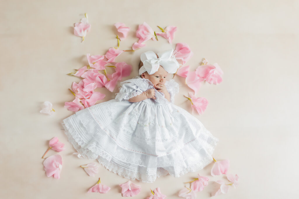 Baby girl laying in lace dress surrounded by flower petals during in-home lifestyle newborn session with 5U Photography in Birmingham AL