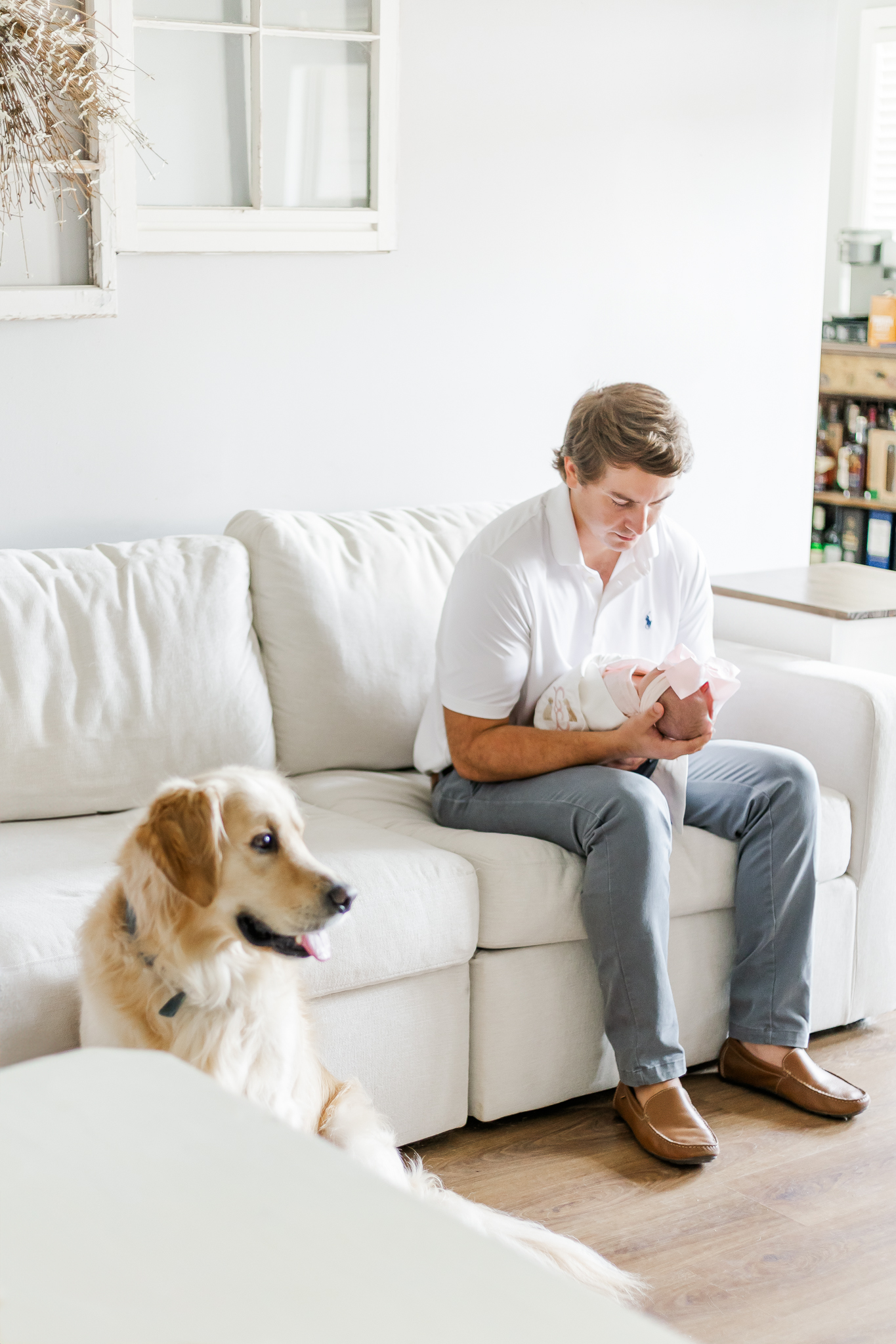 Dad sitting on sofa cradling newborn baby girl wrapped in pink blanket