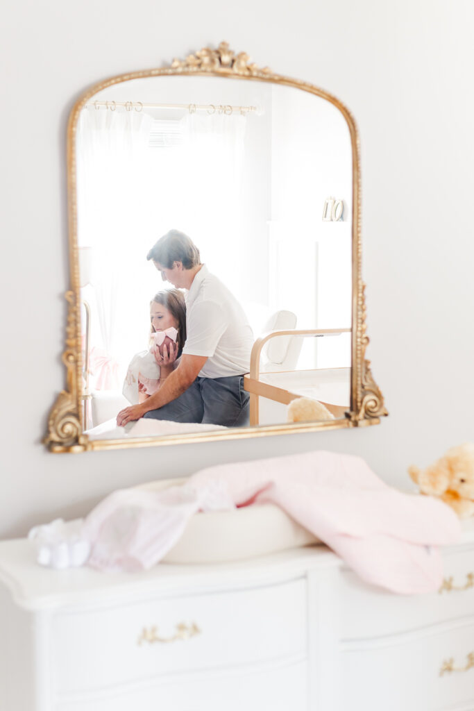 family of 3 sitting in rocker in nursery cradling newborn baby girl