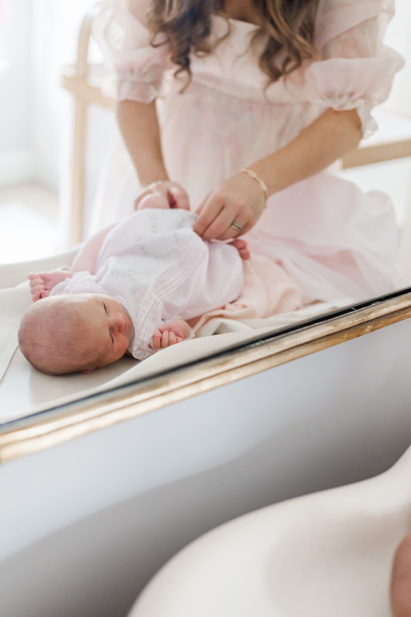 reflection of baby girl in mirror laying on changing table in nursery while mom changes her clothes during newborn session with 5U Photography