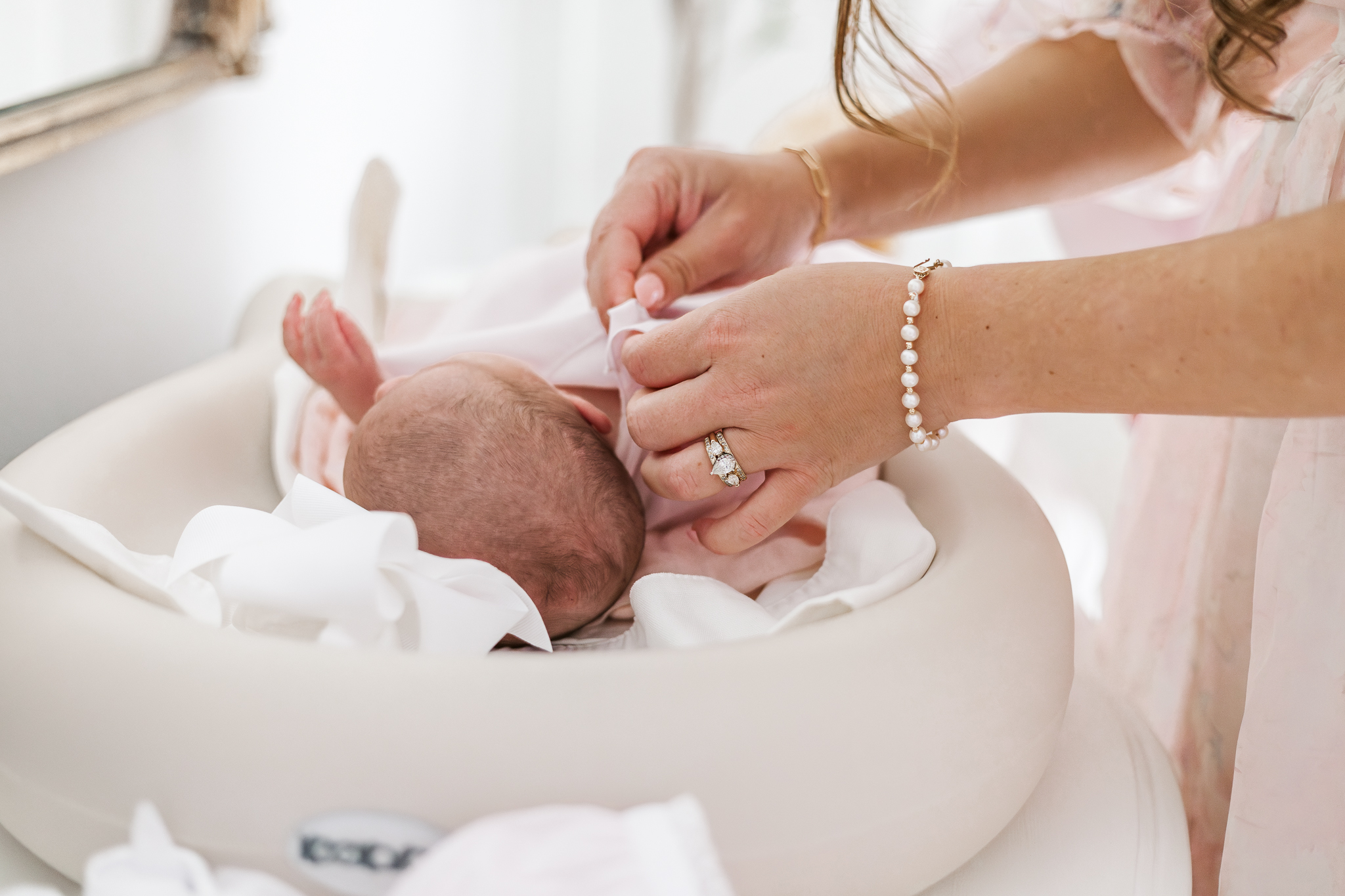 Close-up of a baby girl's tiny hand grasping her mother's finger, captured during an in-home newborn session