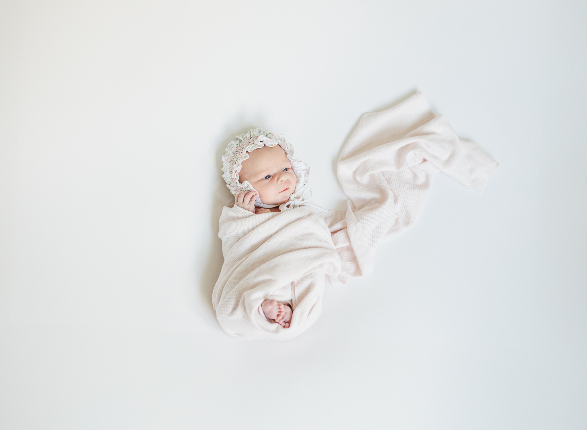 Newborn baby girl swaddled in a floral blanket, lying on a soft rug in a sunlit living room during in-home lifestyle newborn session in Birmingham, Alabama.