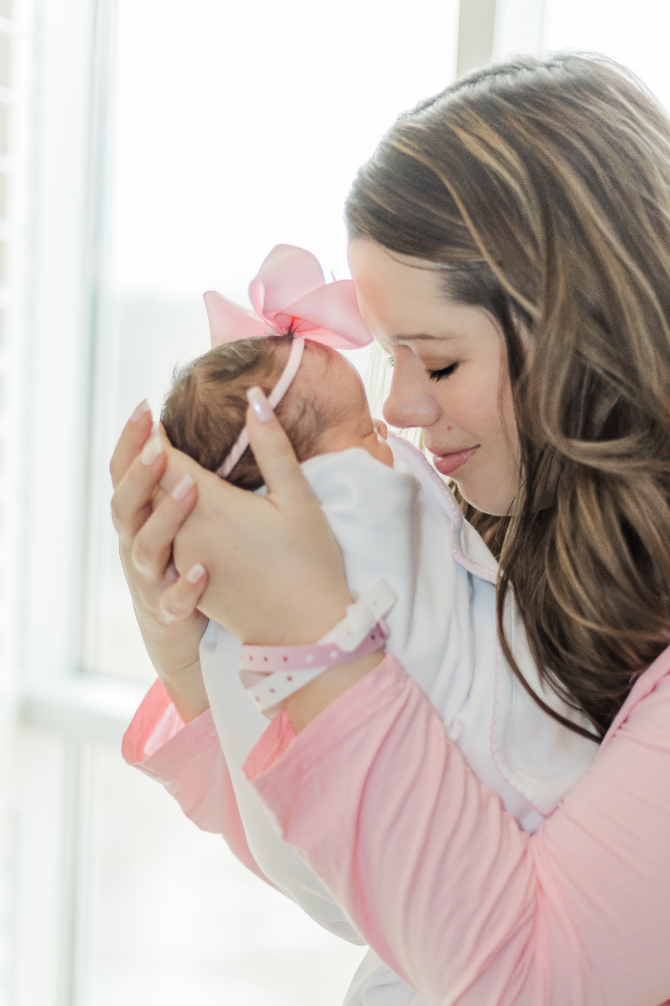 Mom holding newborn baby girl nose to nose with eyes closed in hospital following delivery