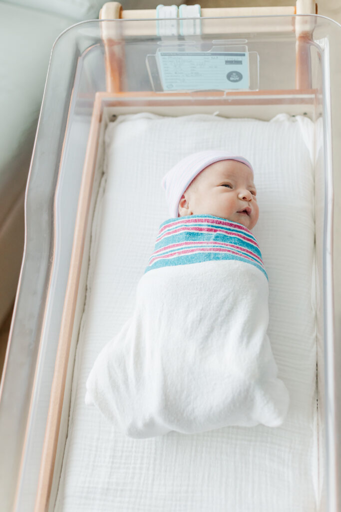 newborn baby boy in hospital swaddle and hat laying peacfully in hospital crib at Grandview Medical Center in Birmingham, AL with eyes open