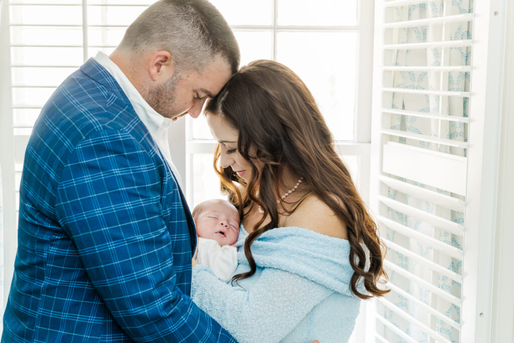 Newborn baby boy sleeping soundly in his mother's arms, with his father gently holding his hand during a cozy winter newborn session.