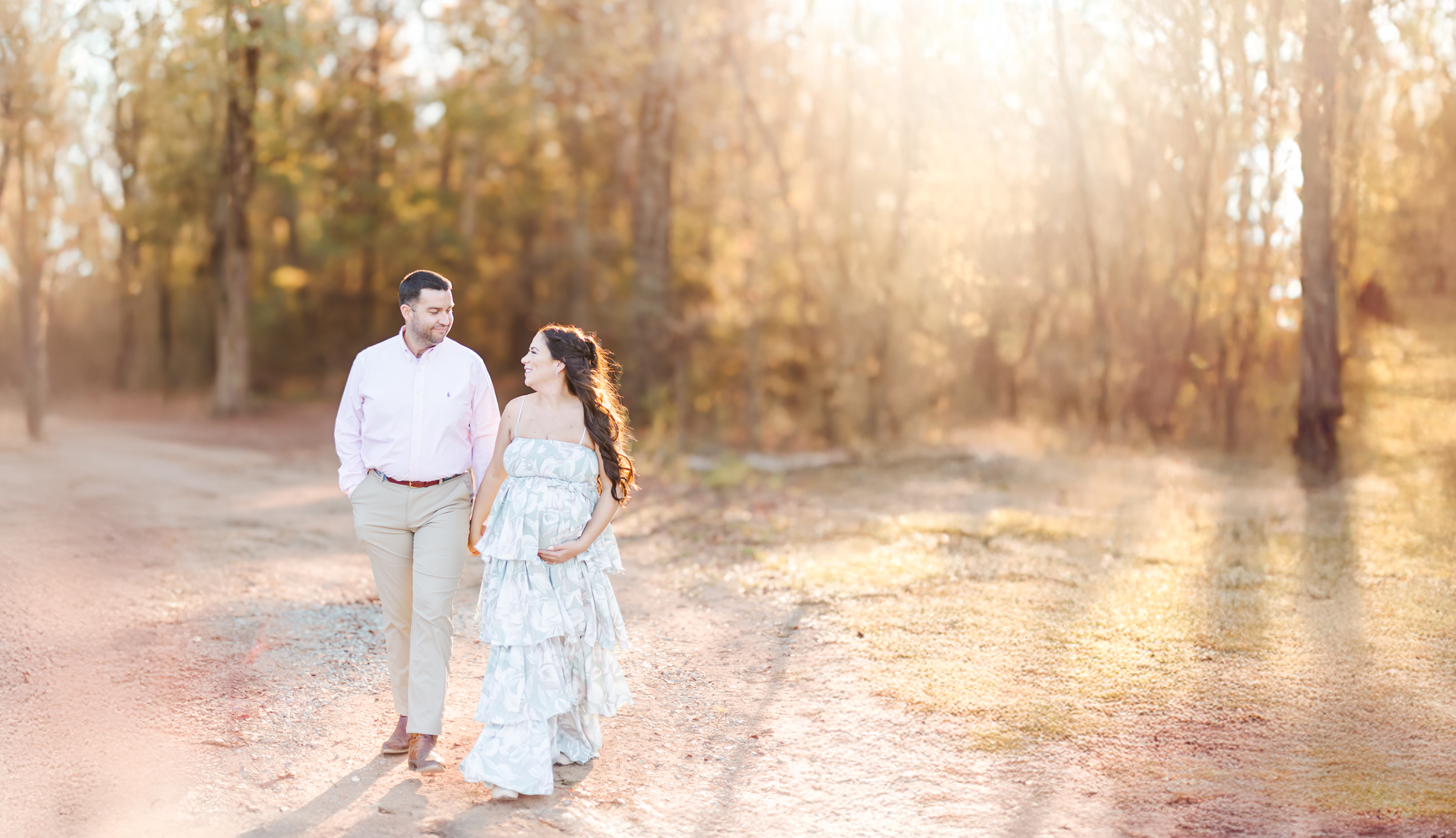 Expecting couple walking hand-in-hand through a picturesque fall field during their maternity session at Old Baker Farm in Birmingham, AL