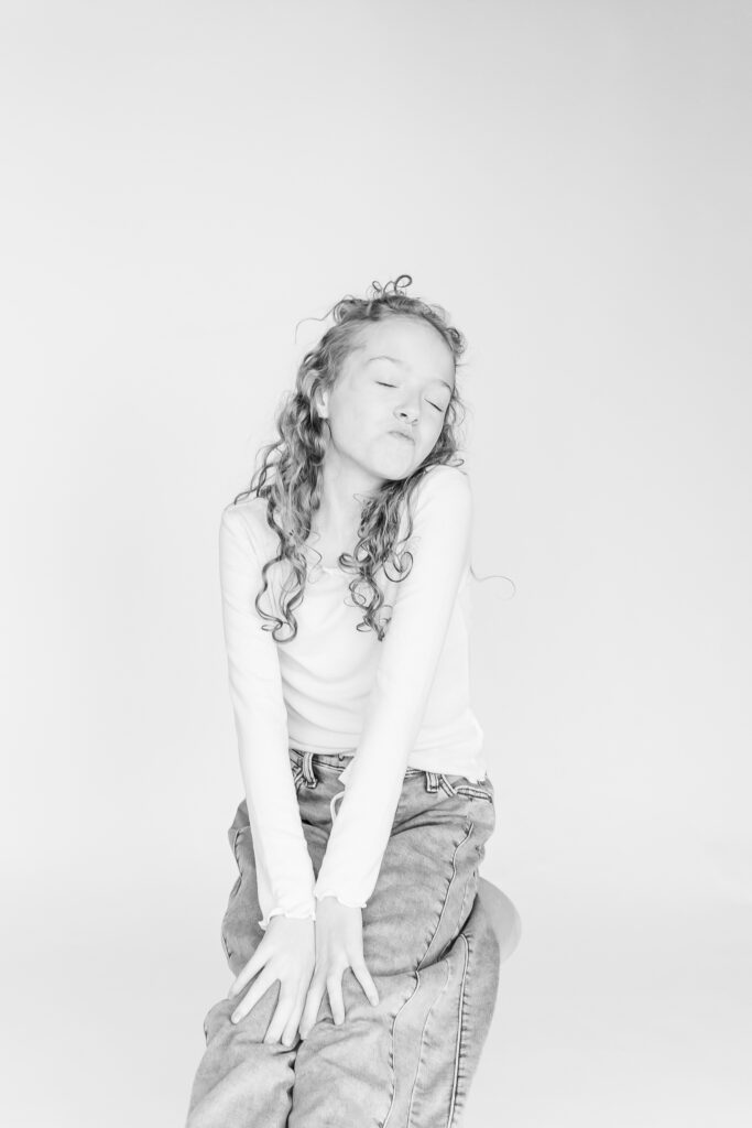 girl sitting on stool with eyes closed and lips pursed during black and white photo session 