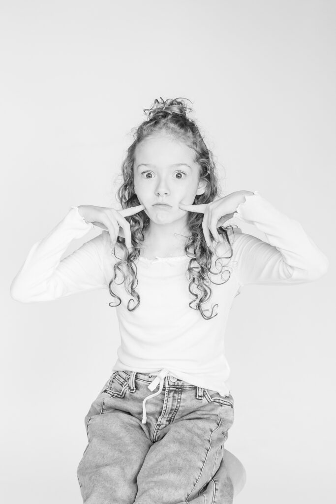 black and white picture of young girl looking at camera while sitting on a stool during photo session 