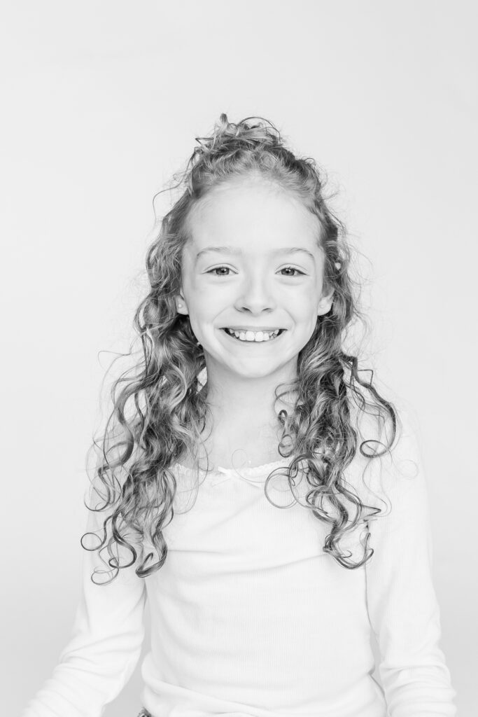 curly hair girl smiling at camera during black and white photo session with 5U Photography 