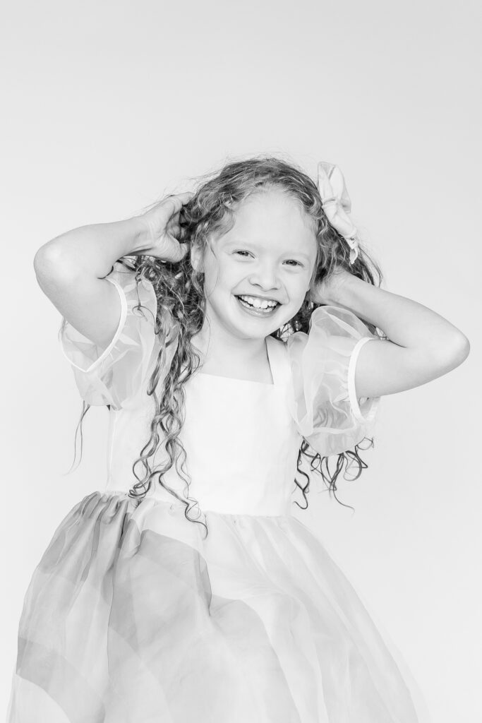 black and white picture of curly haired girl playing with her hair smiling at the camera for portrait with 5U Photography