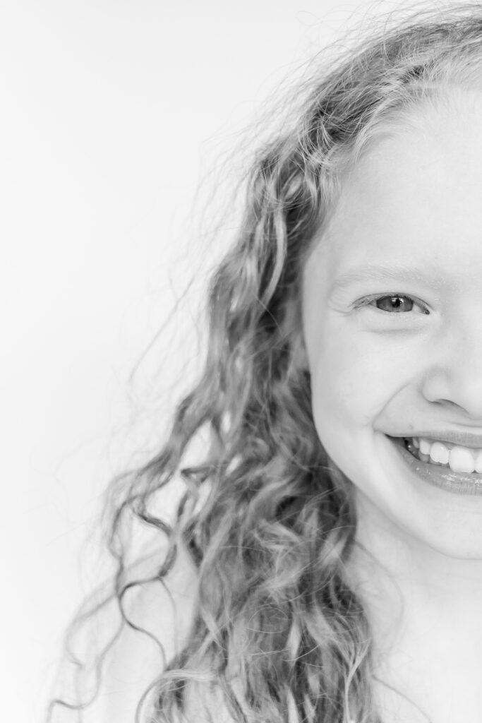 close up black and white image of one half of a little girl's face smiling and looking at the camera during personality portrait party with 5U Photography 