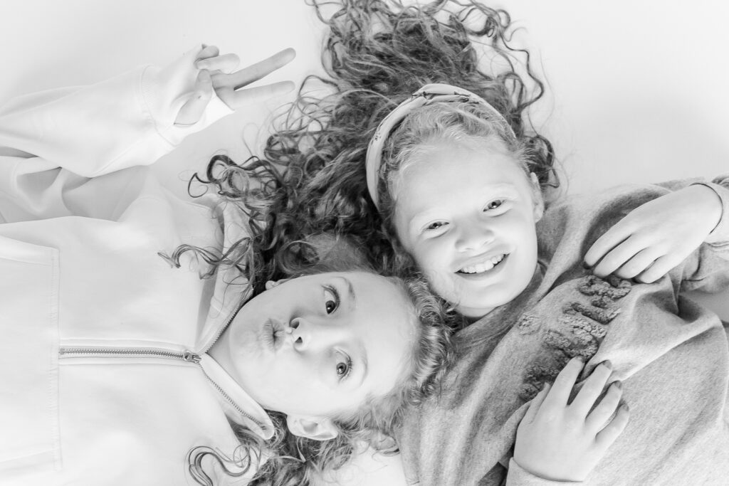 2 sitters lying on the ground with heads together smiling at the camera during a personality portrait party with 5U Photography