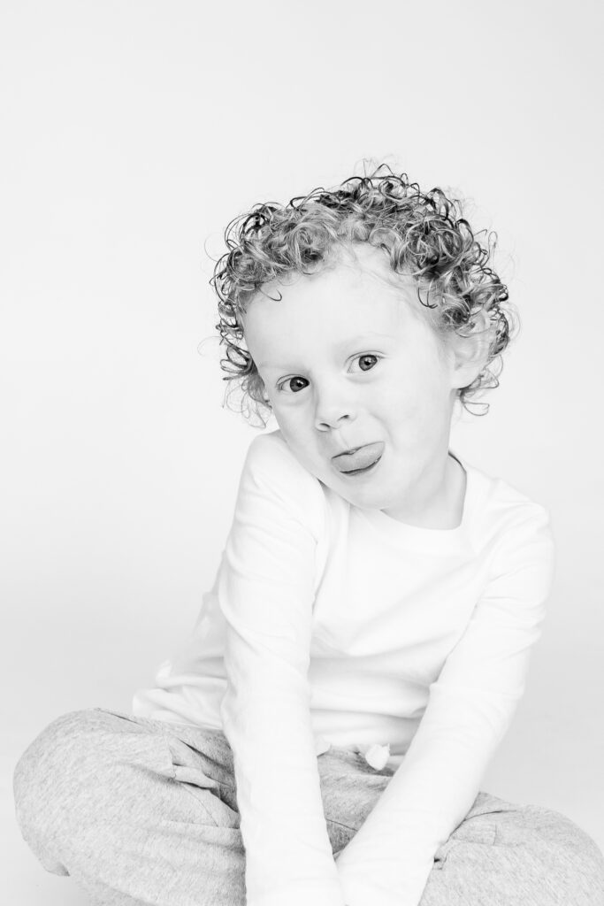 little boy sitting on the floor smiling at the camera with tongue sticking out during personality portrait party in Birmingham 