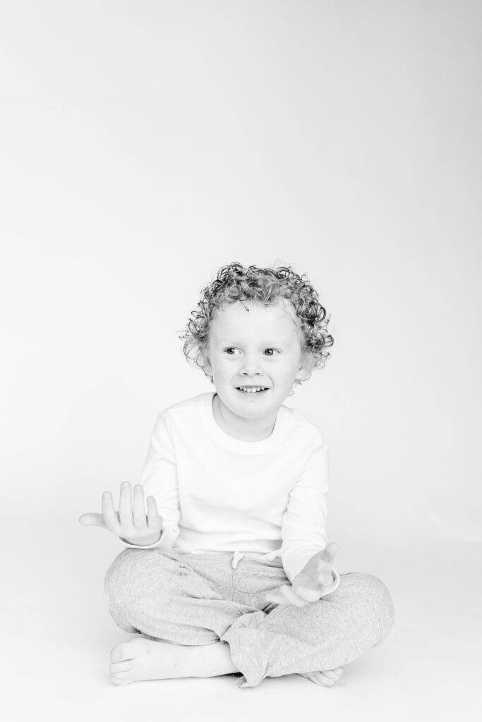 personality portrait of curly haired little boy sitting on ground smiling 