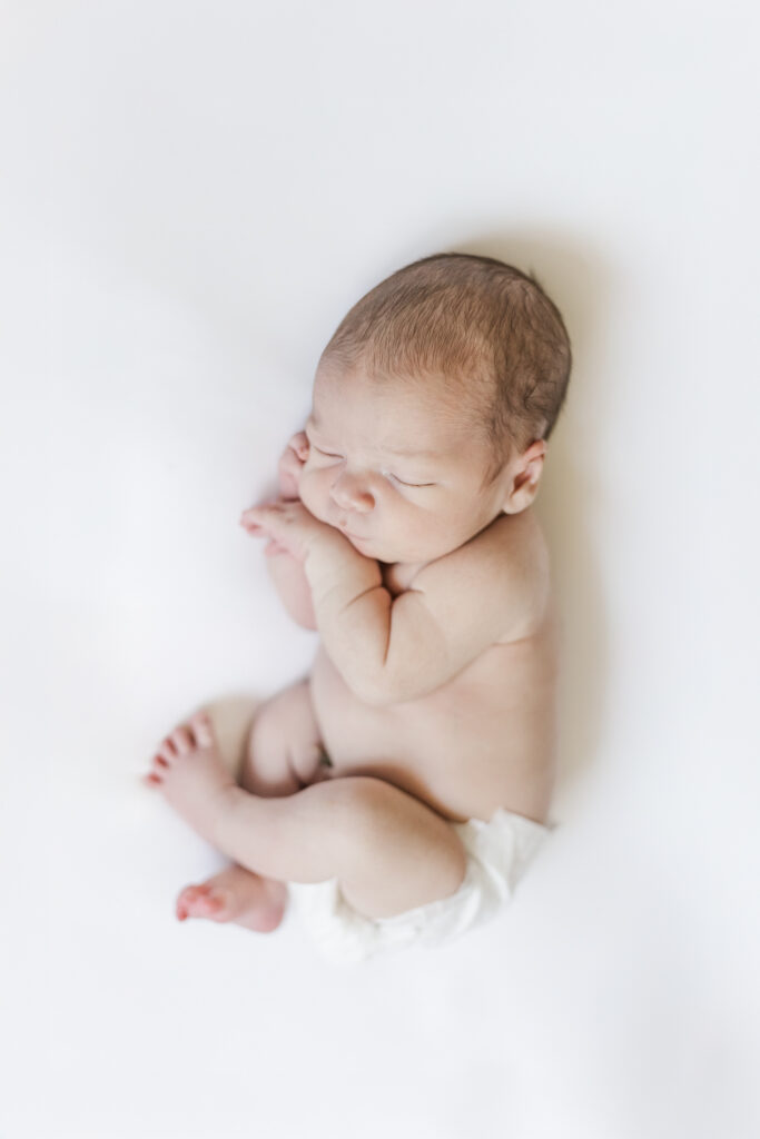 Newborn baby boy laying on white blanket sleeping peacefully with eyes closed during in-home newborn session with 5U Photography