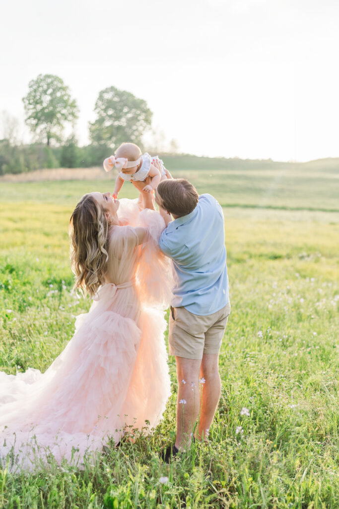 Mom and dad holding 6 month old little girl Daphne in a lush boho field during milestone membership session