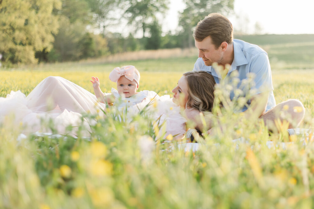 Family sitting on blanket with mom laying against dad holding 6 month old baby girl 