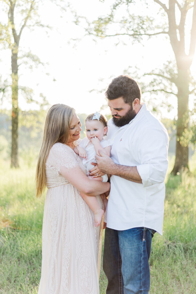 Mom and dad holding 1 year old little girl looking down and smiling during 12 month milestone membership session