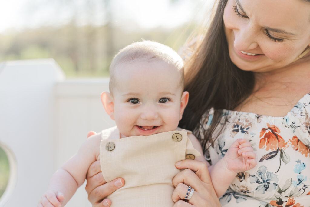 Mom holding little boy smiling at camera during 6 month milestone.