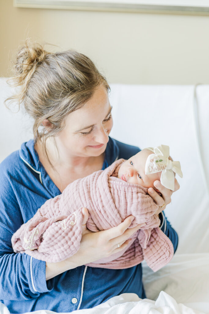 Mom sitting in hospital bed at UAB holding newborn baby girl swaddled in pink blanket during milestone membership included fresh-48 in birmingham alabama