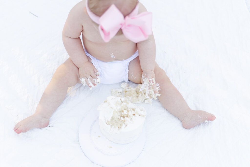 Miss Maggie laughing as she digs into her first birthday cake, creating sweet memories at the Birmingham Botanical Gardens, photographed by 5U Photography