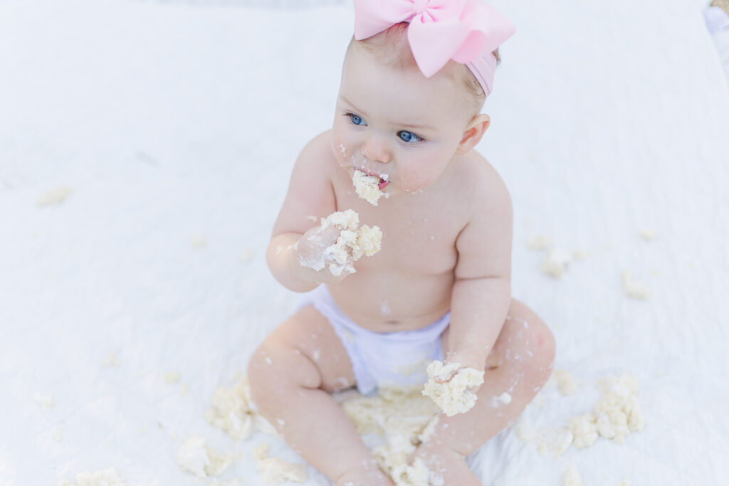 Sweet moment of Miss Maggie with a frosting-covered face, enjoying her smash cake at her first birthday photo session in the Birmingham Botanical Gardens