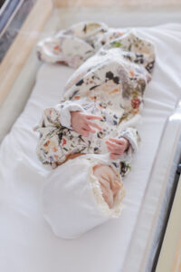 Little girl laying in hospital crib at St. Vincent's Hospital with white bonnet and flowered gown