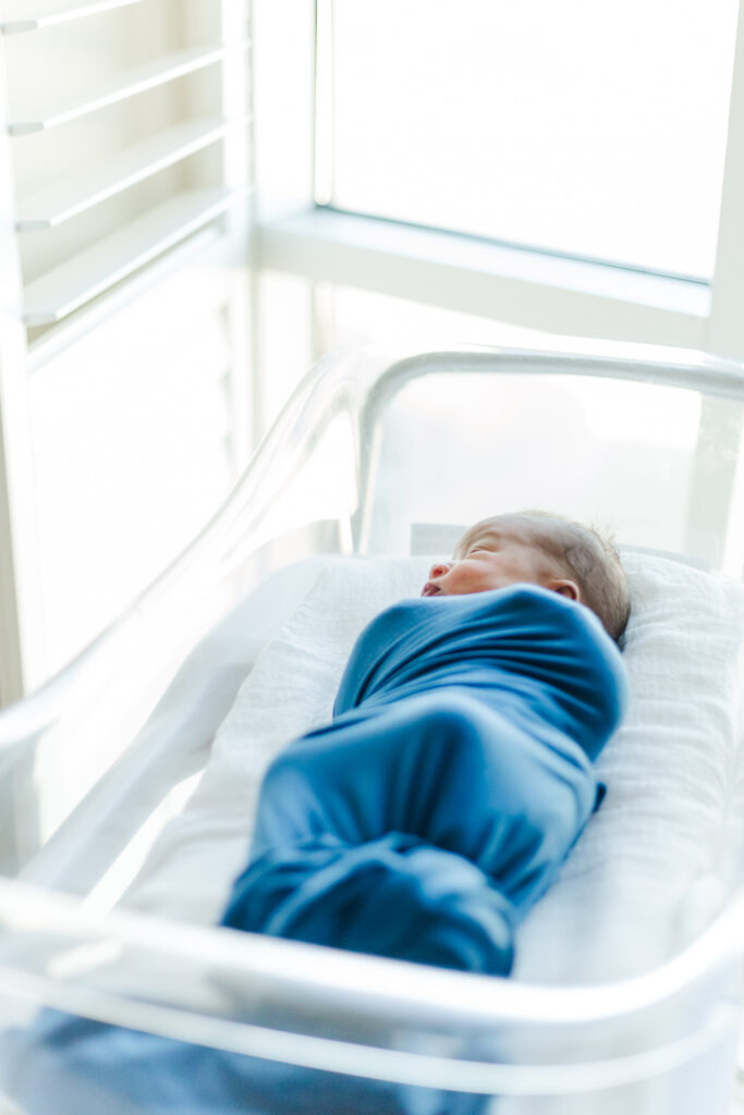 Newborn baby Ezra peacefully sleeping in his hospital crib, wrapped in soft blankets during his Fresh 48 session