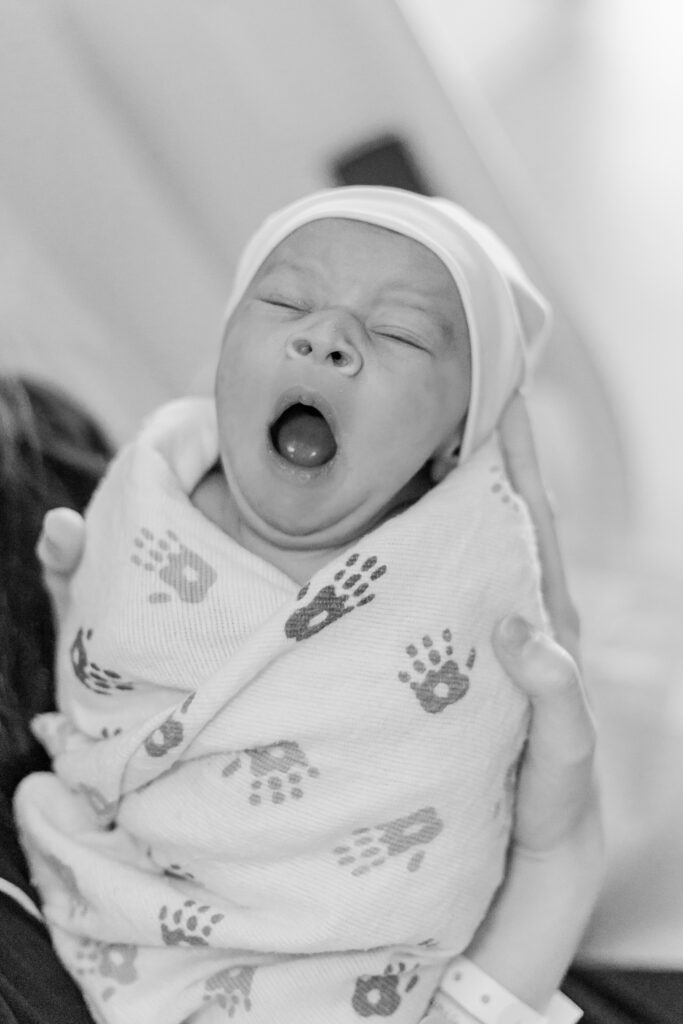 Newborn baby Ezra stretching his arms and yawning, a precious moment during his Fresh 48 session