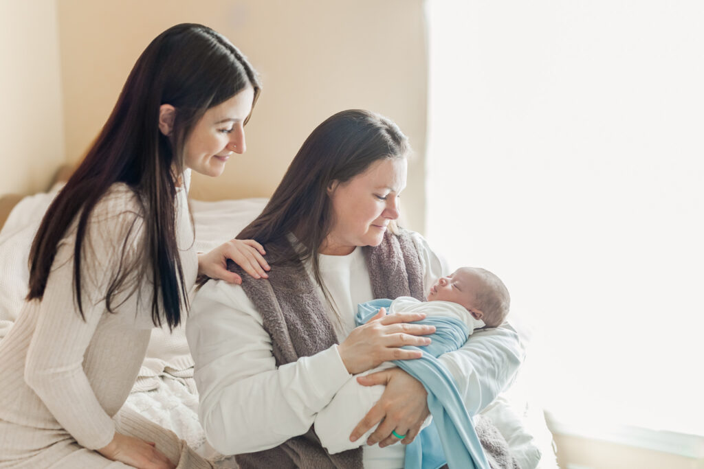 Family portrait featuring mom Kinsley, baby Ezra, grandmother Nonni, and Uncle 'Unc Unc' in a cozy in-home newborn photoshoot