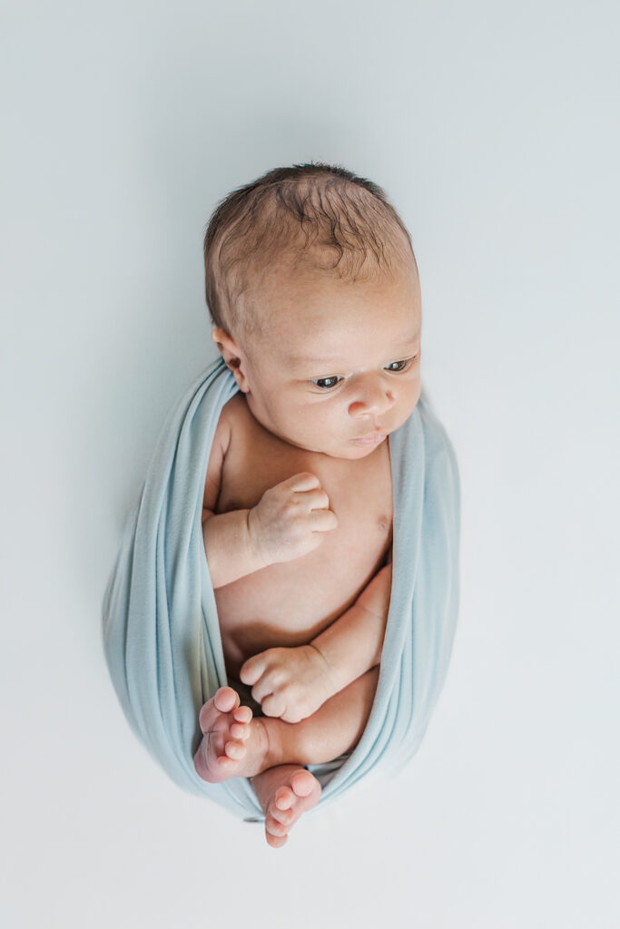 newborn baby boy wrapped in blue swaddle during cozy in-home newborn session