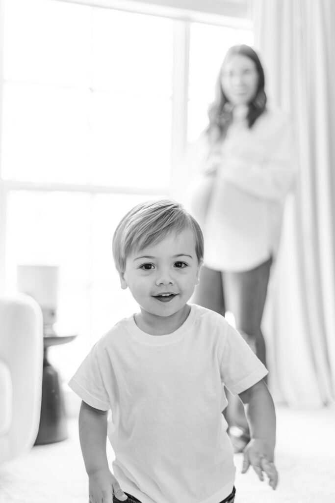 black and white picture of boy staring at the camera with pregnant mom in the background during session with 5U Photography in Birmingham AL