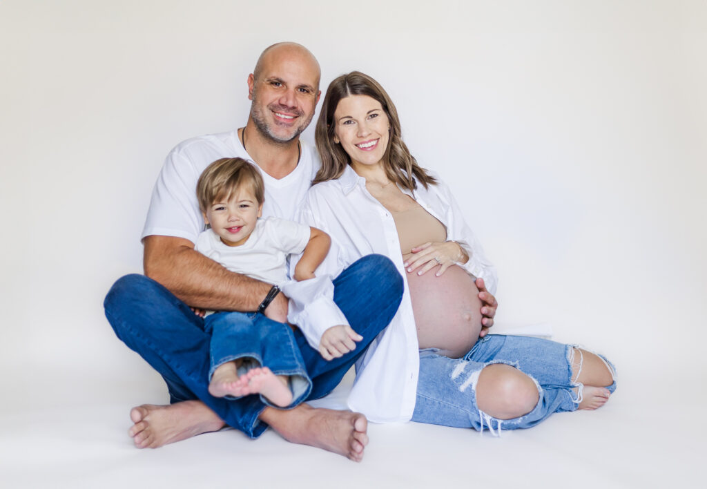 A candid moment of the Lavender family embracing each other with joyful smiles as they celebrate the arrival of their baby sister, set against a simple, elegant portable backdrop