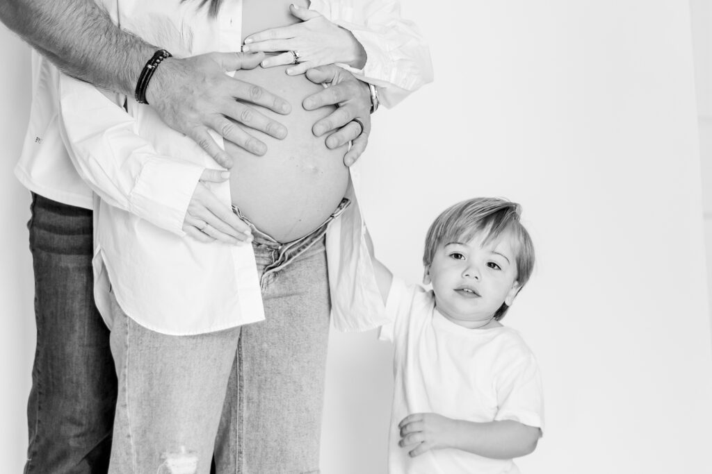 close up of big brother with hands on mom's belly during an in-home maternity session