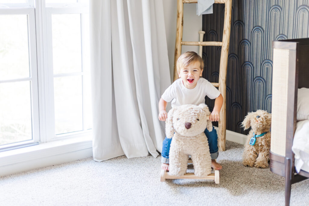 Little boy laughing at camera on rocking dog toy at his home in Birmingham, AL