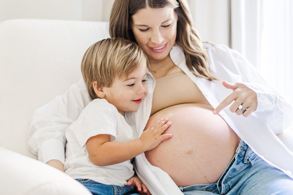 Picture of toddler boy with hand on expecting mom's baby bump during in-home maternity session with 5U Photography in Birmingham, AL