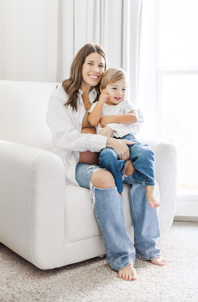 The Lavender family posing together in front of a soft, neutral-toned portable backdrop during their in-home maternity session, with the soon-to-be big sibling smiling excitedly about their new baby sister.