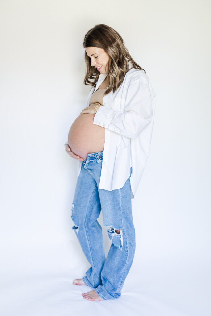 A beautiful full-body shot of the mother in a flowy maternity dress, posed against a simple backdrop, capturing the peaceful moments of her in-home session in Birmingham with 5U Photography