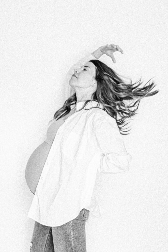 candid black and white picture of mom tossing her hair back with pregnant belly showing during in-home maternity session