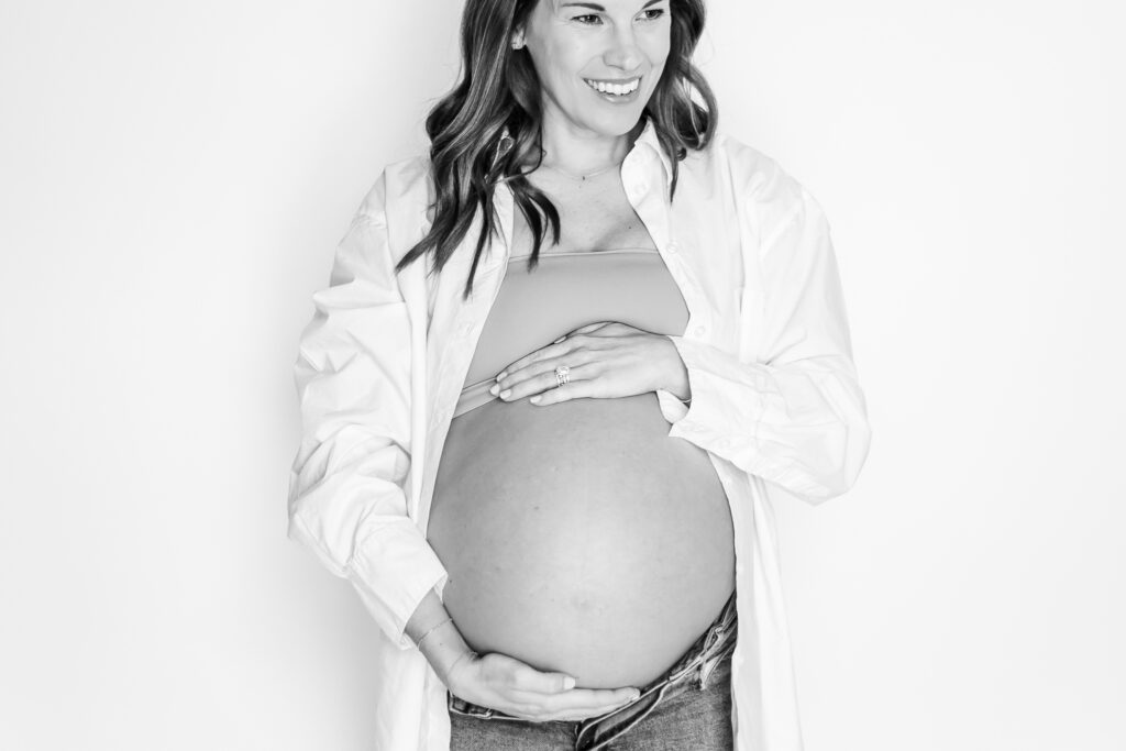 close up black and white picture of pregnant mom holding her belly smiling during in-home maternity session with 5U Photography