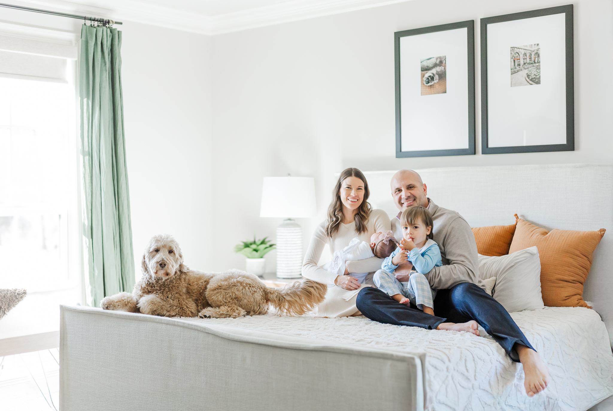 Family sitting on bed smiling at the camera during in-home newborn session with 5U Photography