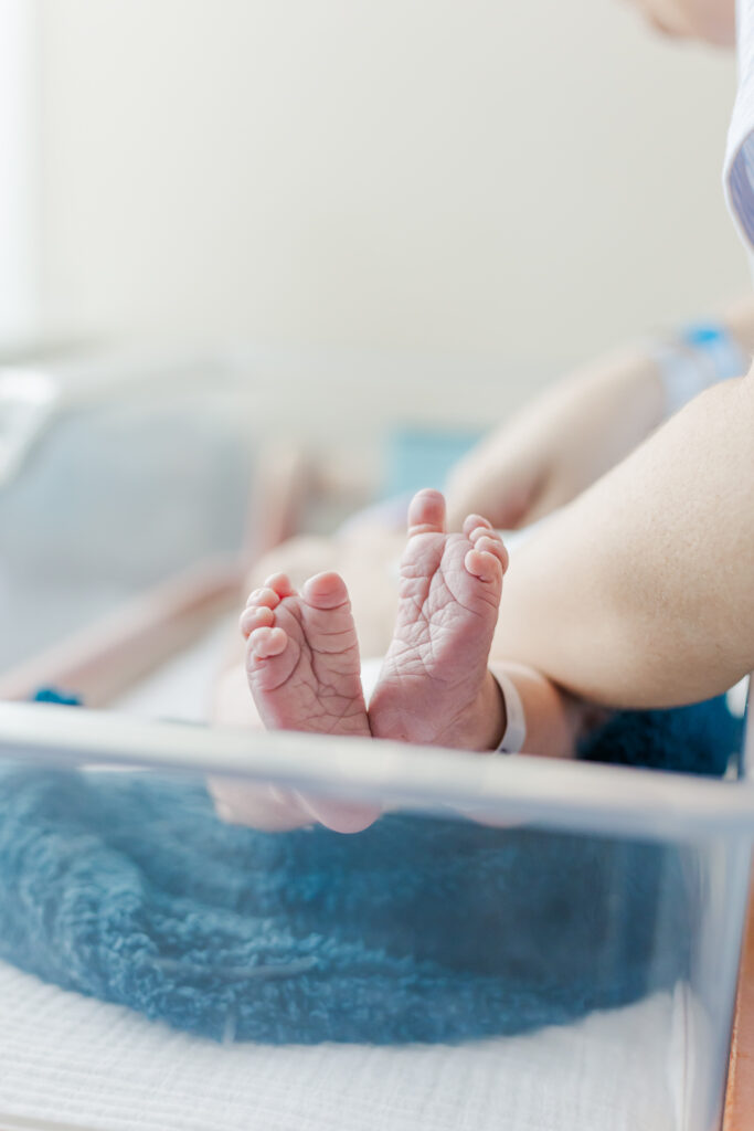 close up of baby boy's feet lying in hospital crib while being swaddled by mother during fresh-48 session