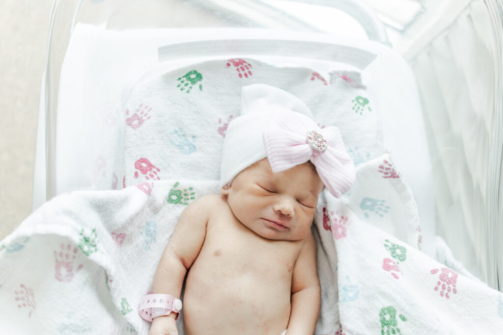 close up of baby girl laying in hospital crib with hat on at Brookwood Hospital 