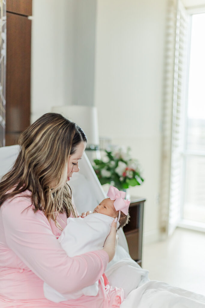 Mom sitting in hospital bed looking down at baby girl following delivery during milestone membership fresh-48 session at brookwood hospital in Birmingham, AL 