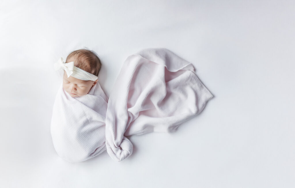 newborn baby girl wrapped in pink swaddle with white boy sleeping peacefully during newborn session wtih 5U Photography