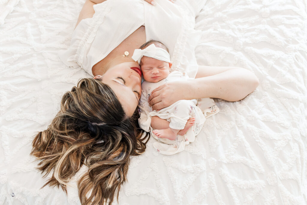 Mom laying on bed with newborn daugher snuggled by her face in a tender moment during photo session with 5U Photography