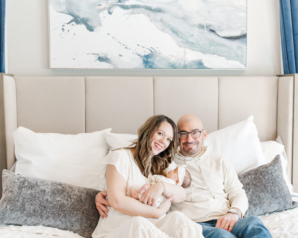 Mom and dad sitting on their bed in Gardendale, AL smiling at camera during newborn session 