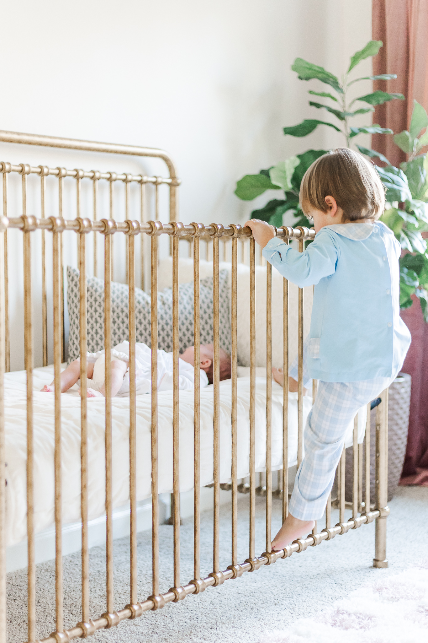 Little boy climbing on crib looking down at baby sister at the family's home in Birmingham, AL 